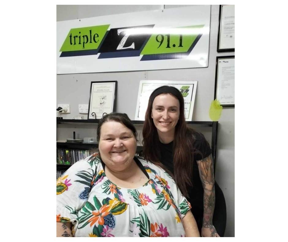 Two women, one sitting and one standing smiling into the camera